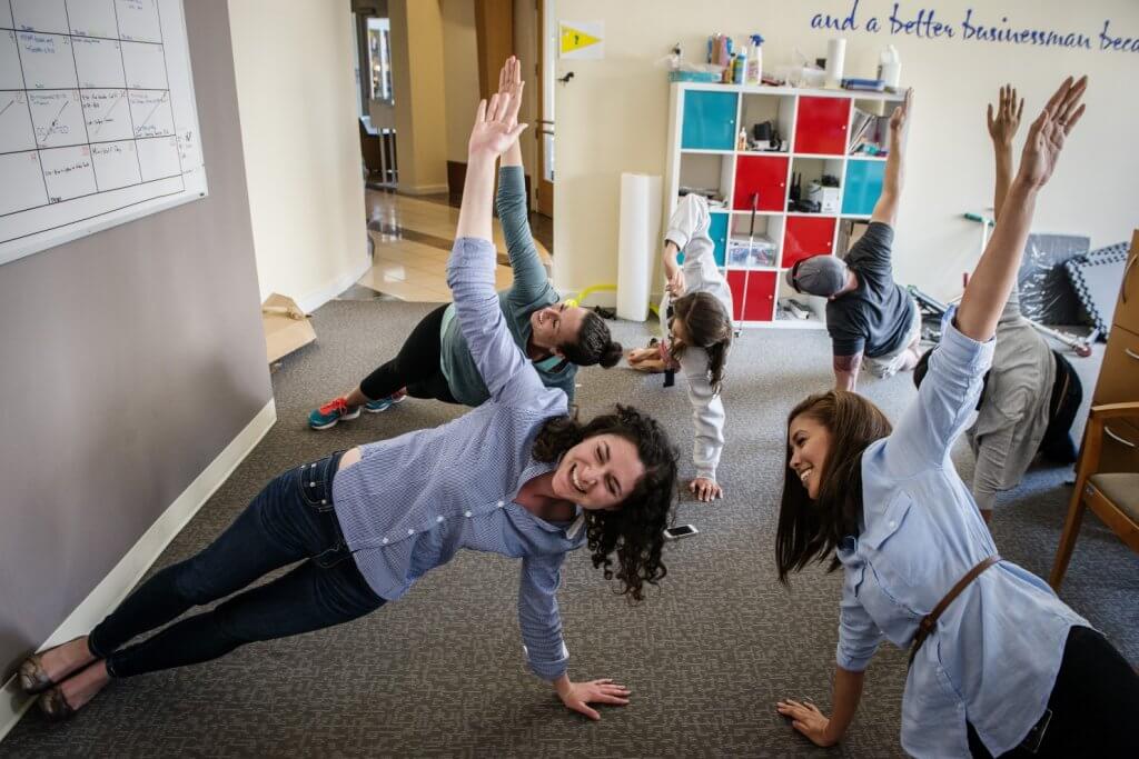 Employees participating in their employee wellness program in office as they stretch on the ground.