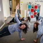 Employees participating in their employee wellness program in office as they stretch on the ground.