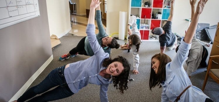 Employees participating in their employee wellness program in office as they stretch on the ground.