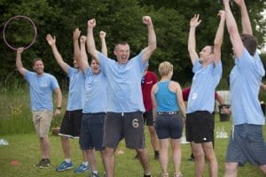 Adults in matching blue shirts celebrating their win of an outdoor yard game.