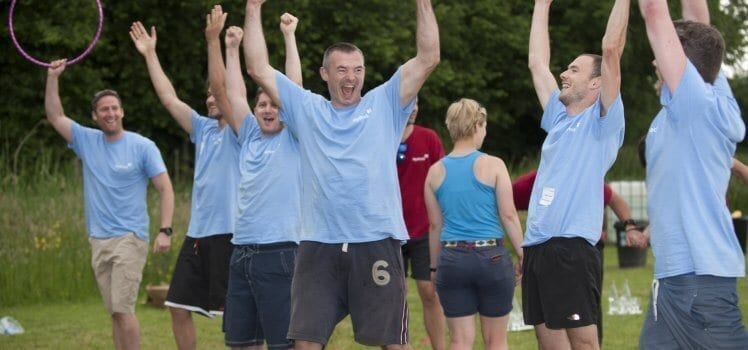 Adults in matching blue shirts celebrating their win of an outdoor yard game.