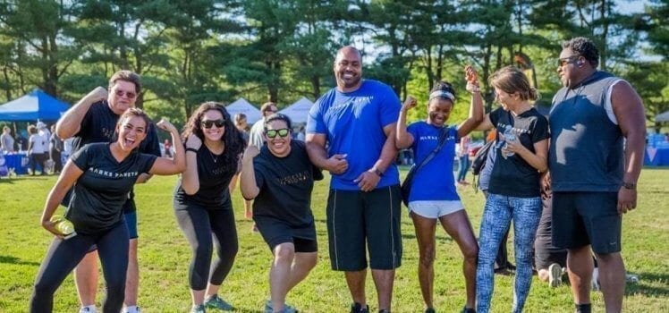 Group of coworkers standing in a line smiling and laughing as they show their muscles off.