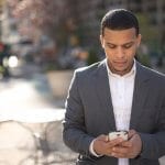 Man in a suit holding his phone outdoors in the city.