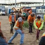 Construction workers in hard hats and safely vests doing stretches prior to beginning their day.