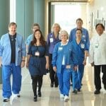 Group of medical professionals in blue or white walking down a medical office hallway.