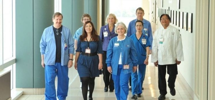 Group of medical professionals in blue or white walking down a medical office hallway.
