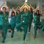 Group of medical professionals in blue scrubs going yoga in a hallway of the medical building.