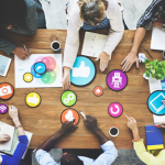 Overhead view of workers sitting around a table point to various graphical images.