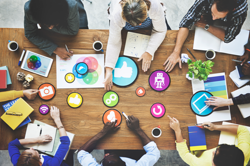 Overhead view of workers sitting around a table point to various graphical images.