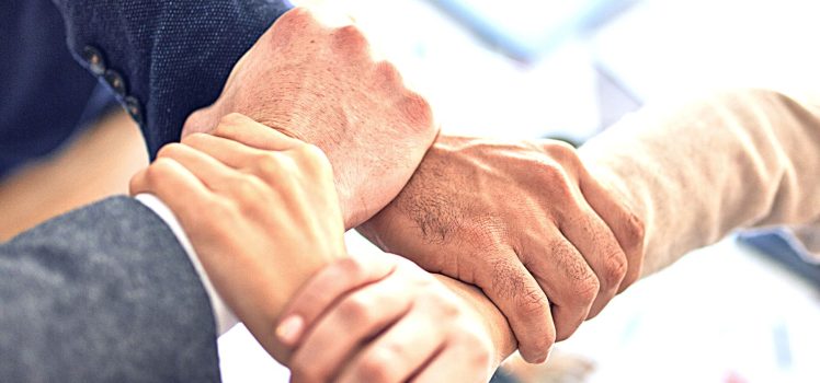 Group of four people holding another's wrist to make a square. 13 Fun Workplace Wellness Challenge Ideas Your Employees Will Enjoy