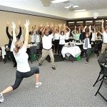 Large group of workers doing group stretches at a conference. workplace health promotion program