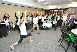 Large group of workers doing group stretches at a conference. workplace health promotion program