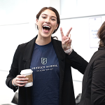 Happy young woman doing the peace sign with her hands as she holds a hot drink and smiles.