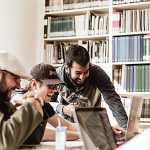 Group of three man laughing and happy while looking at something on a shared laptop screen.