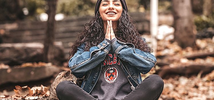 Young woman sitting on the ground outside meditating and smiling. benefits of meditation and mindfulness