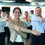 Group of office workers gathered together doing arm stretches and smiling.