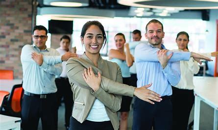 Group of office workers gathered together doing arm stretches and smiling.