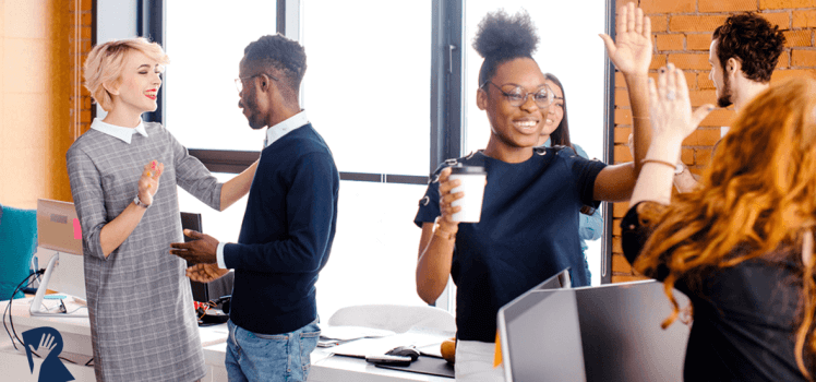 Group of people celebrating in an office with high fives and hugs.