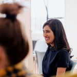 Woman in a blue shirt in an office setting laughing.