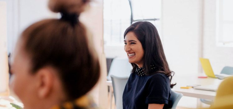 Woman in a blue shirt in an office setting laughing.