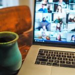 Computer screen showing a video call with many different attendees and a mug on the table.