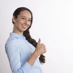 Woman in a blue shirt looking at the camera giving a thumbs up with her hand.