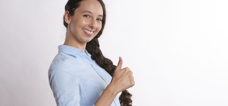 Woman in a blue shirt looking at the camera giving a thumbs up with her hand.