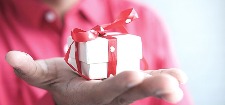 Closeup of a person in a pink shirt holding a very small white box with red ribbon and white hearts.
