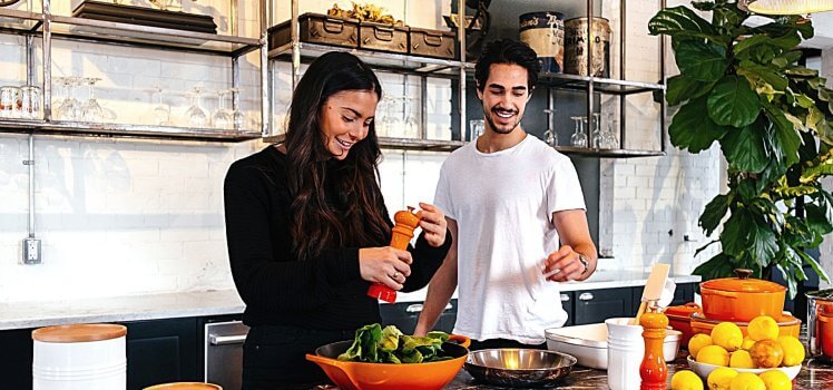 Two people preparing a salad in a large bright kitchen.