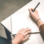 Close up of a woman in a brown sweater holding a pen beginning to write in a journal. Questions to ask while evaluating a wellness program