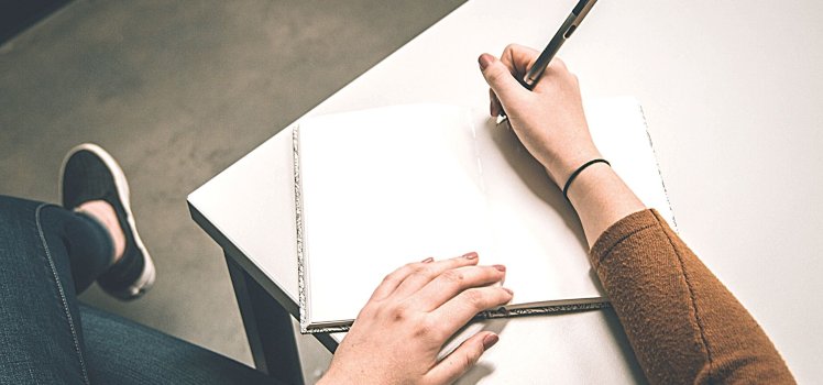 Close up of a woman in a brown sweater holding a pen beginning to write in a journal. Questions to ask while evaluating a wellness program