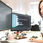 Side profile of a woman with red hair working at a desk with three large screens.