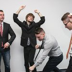 Four men in business attire dancing in celebration.