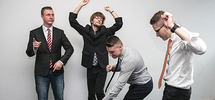 Four men in business attire dancing in celebration.