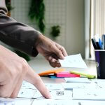 Sideview of a person placing sticky notes on a table with a cup of pens.