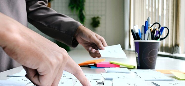 Sideview of a person placing sticky notes on a table with a cup of pens.