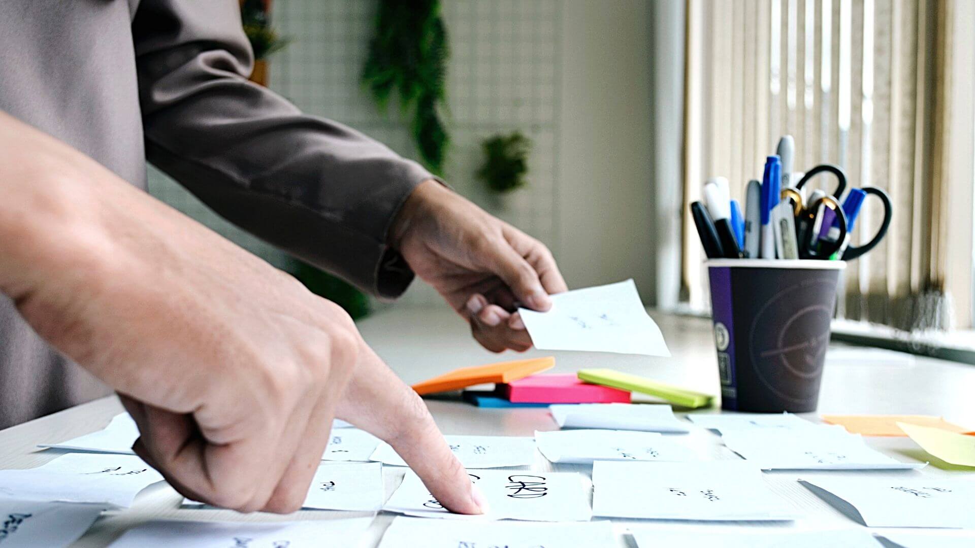 Sideview of a person placing sticky notes on a table with a cup of pens.