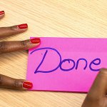 Person writing the word DONE on a bright pink sticky note.