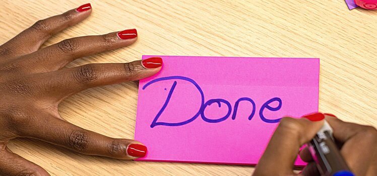 Person writing the word DONE on a bright pink sticky note.