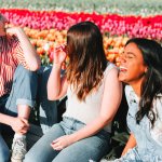 Three women sitting on a bench laughing in front of a large field of tulips.