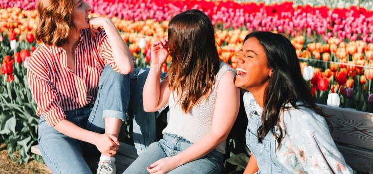 Three women sitting on a bench laughing in front of a large field of tulips.