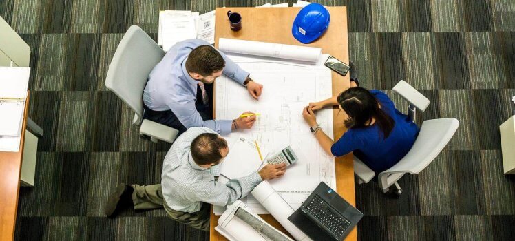 Overhead view of three people marking a building schematic displayed on a large table.