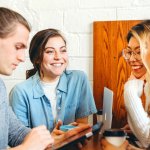 Group of people standing closely talking and laughing. 19 Healthy Work Environment Examples to Upgrade Your Employees Physical Well-Being