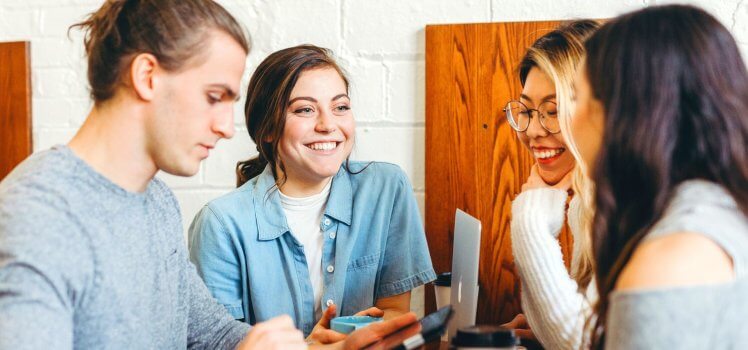 Group of people standing closely talking and laughing. 19 Healthy Work Environment Examples to Upgrade Your Employees Physical Well-Being