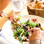 Closeup of a person eating a fresh salad with a basket of fresh bread on the table.