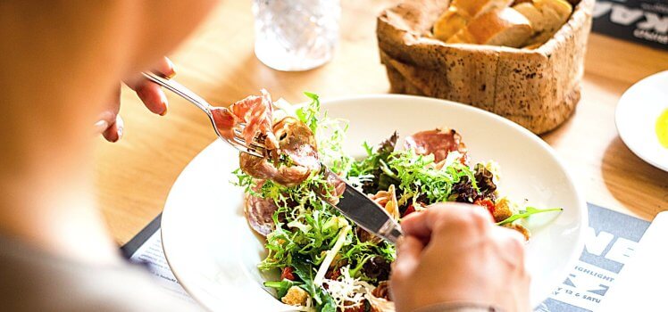 Closeup of a person eating a fresh salad with a basket of fresh bread on the table.