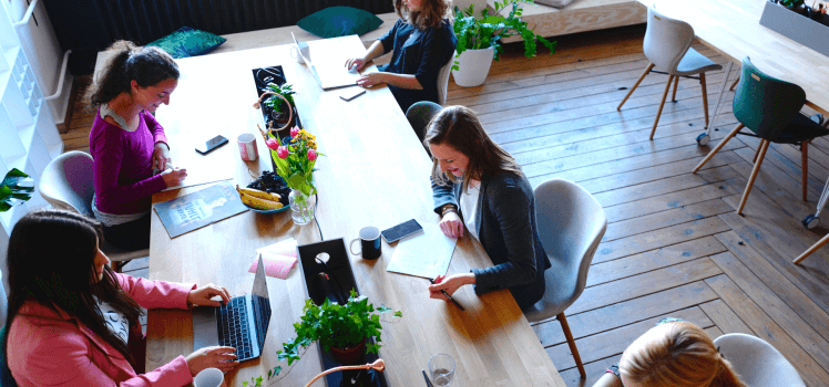 Overhead view of five women working independently with computers at a large table.