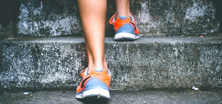 Closeup of person in blue and orange shoes climbiing up stairs. Easy ideas for increased fitness in the workplace