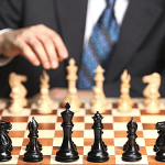 Man in black with a blue tie playing chess, from the opponents viewpoint.