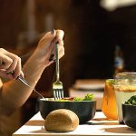 Closeup profile view of a person eating a salad on a table.